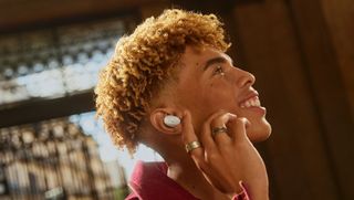 White Sennheiser Accentum earbuds, worn by young adult in red shirt